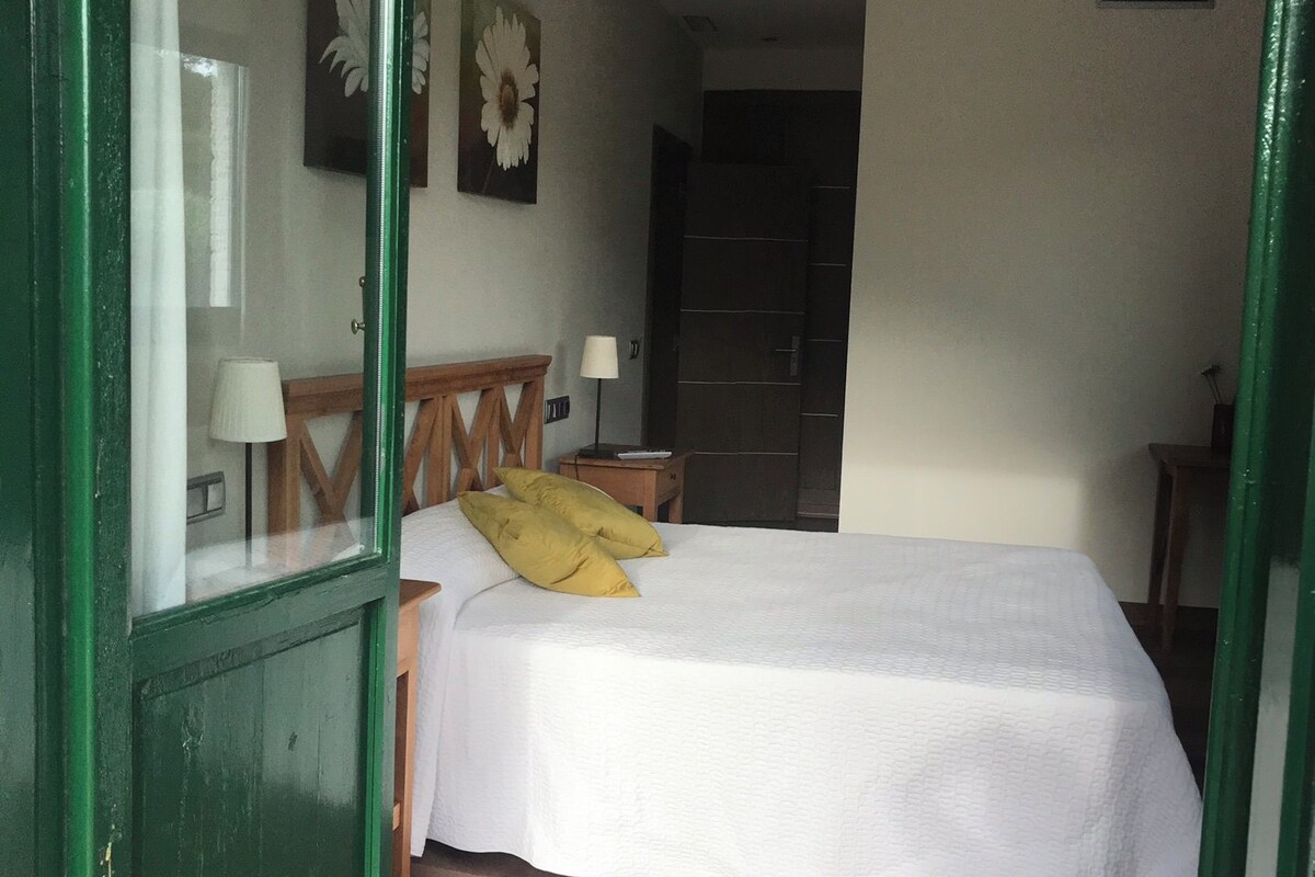 A bedroom with a bed, a wooden headboard, two bedside lamps, and a door leading to another room.