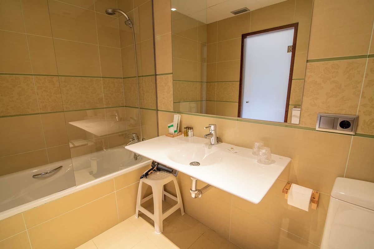 Un baño con ducha de vidrio, un lavamanos blanco con un espejo encima y un inodoro.