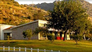 A two-story stone building with a flat roof, surrounded by a white picket fence, set against a hilly backdrop. - Hotel Rural Aldeaduero (Saucelle)