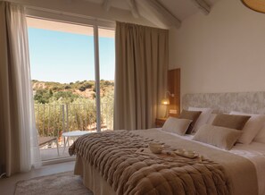 A bedroom with a large bed, a nightstand, a lamp, and a view of a hillside through a sliding door. - Hacienda Fresneda María by Real Spain Hotels (Antequera)