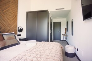 Ein Hotelzimmer mit Bett, Schrank, einer kleinen Bank, einem runden Hocker und einem Flachbildfernseher an der Wand.