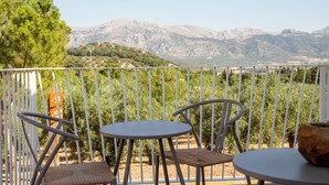 En balkon med to stole og et bord, med udsigt over et bjergrigt landskab.
