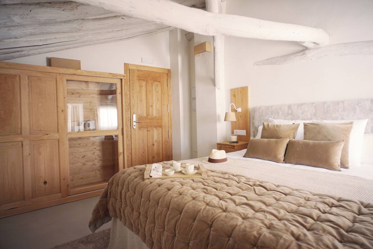 A bedroom with a large bed, wooden wardrobe, and a nightstand with a lamp.