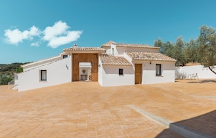 Una villa blanca con techo de tejas, un porche cubierto y un patio empedrado.