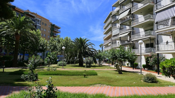 A courtyard with a paved walkway, palm trees, and a multi-story building with balconies. - Rentalmar Aries Plus (Salou)