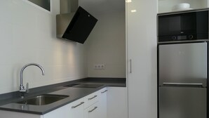 A modern kitchen with a stainless steel sink, a built-in oven, and a refrigerator. - Rentalmar Aries Plus (Salou)