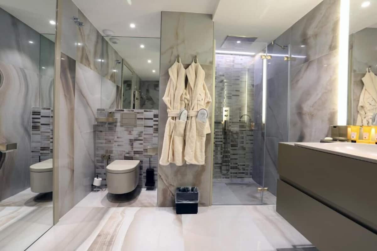 A modern bathroom with a marble backsplash, a glass shower enclosure, and a vanity with a mirror.