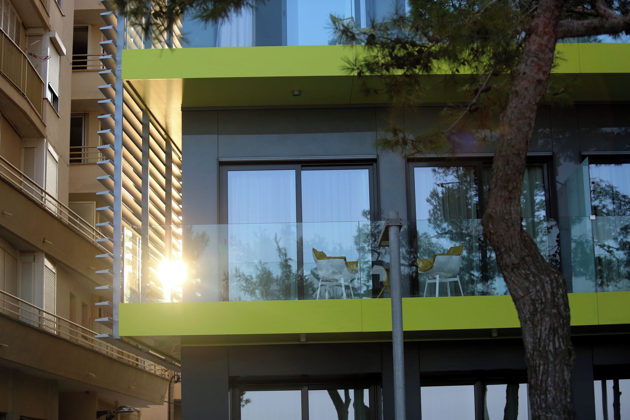 Un edificio moderno con balcón, ventanas amplias y un árbol en primer plano.