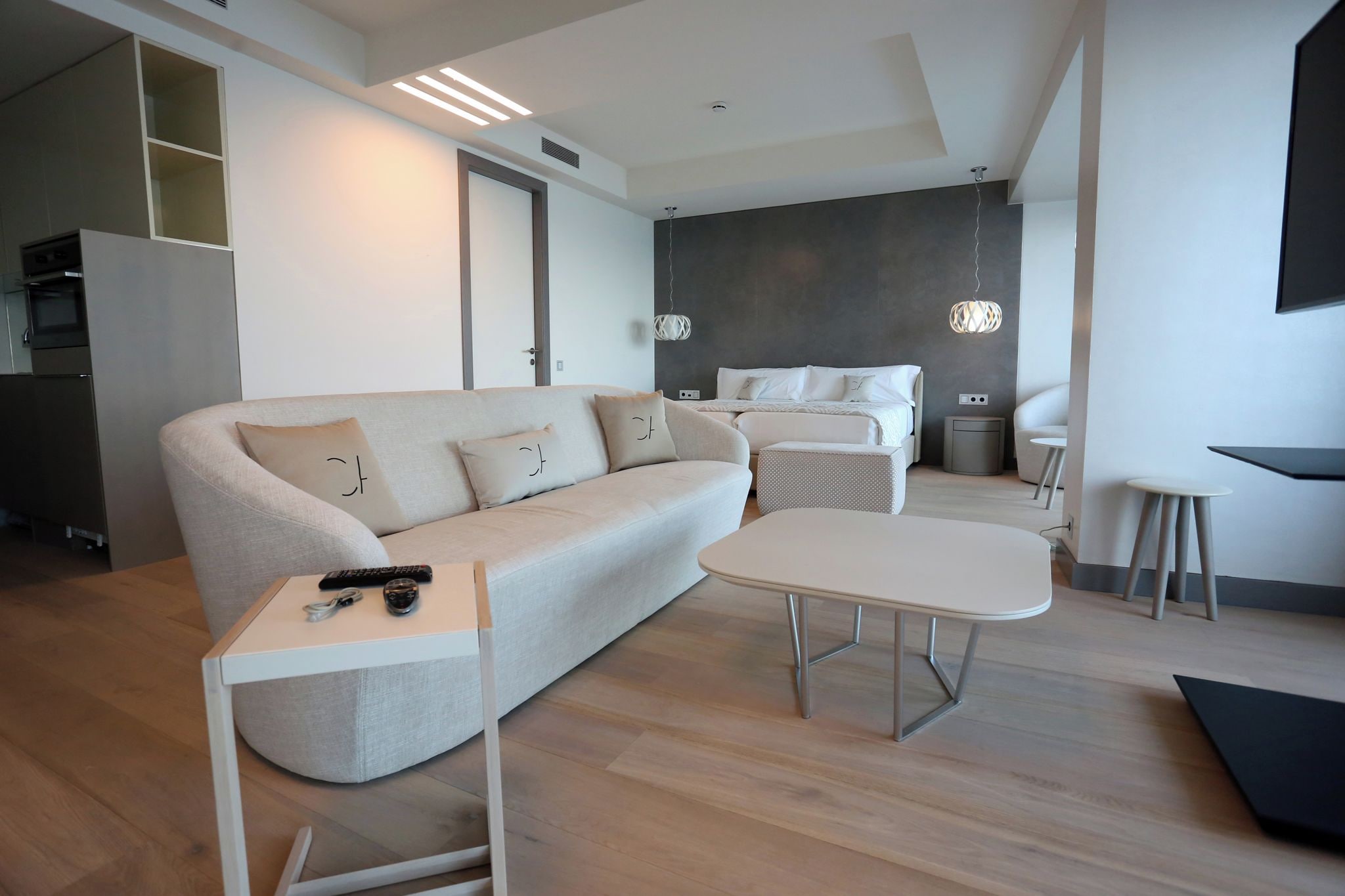 Una sala de estar moderna con un sofá, una mesa de centro y un televisor. Hay una zona de cocina con armarios y un microondas.