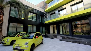 Un edificio moderno con un letrero que dice "APARTMENT" y dos coches amarillos estacionados frente a él.