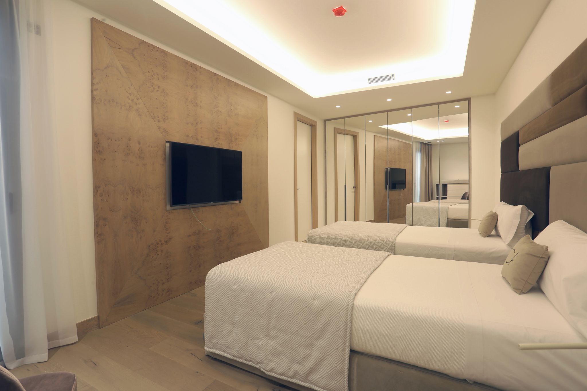 Una habitación de hotel moderna con dos camas, un televisor de pantalla plana montado en la pared y un espejo grande que refleja la habitación.