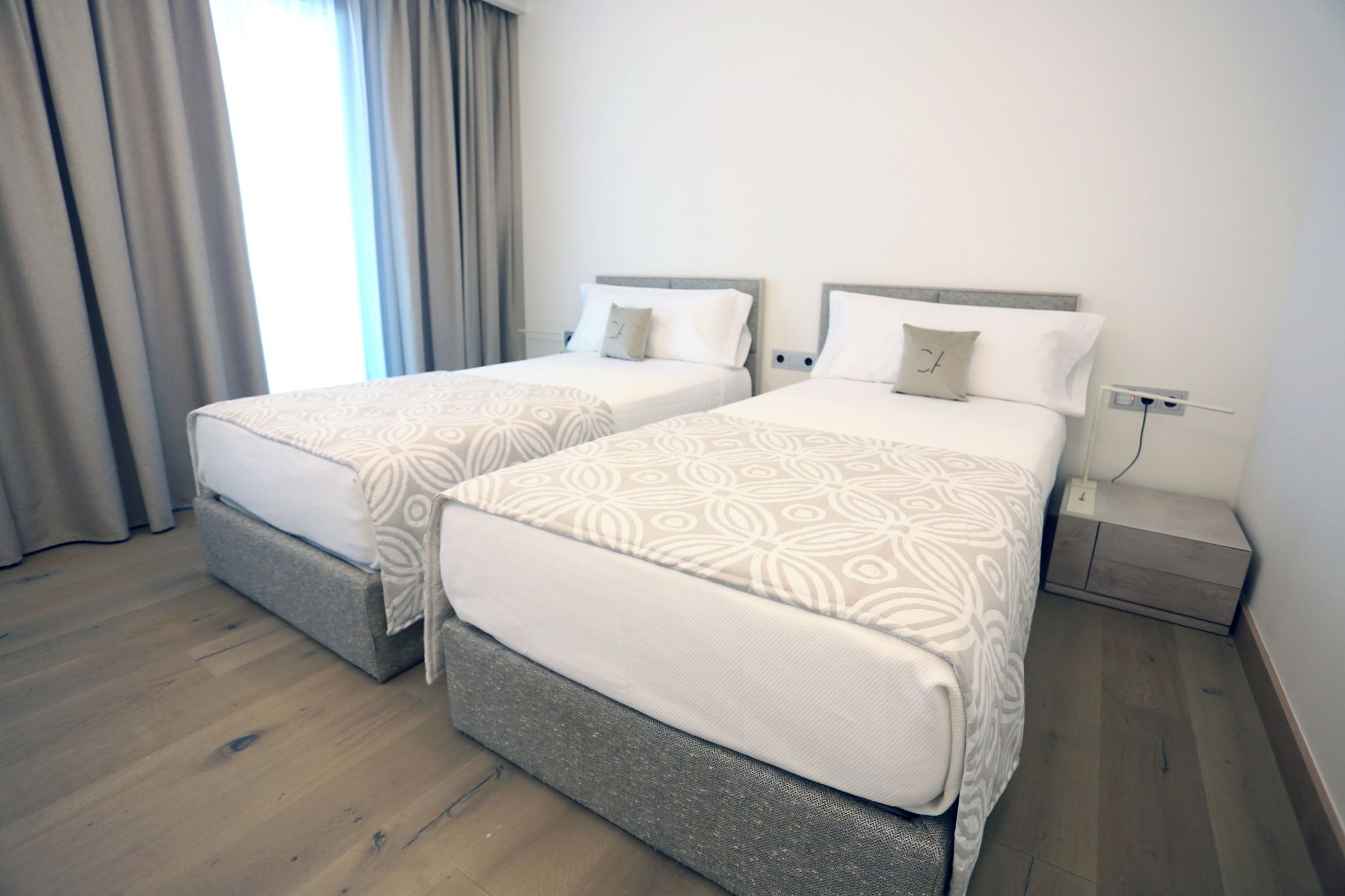 Habitació d'hotel amb dos llits, cadascun amb un estriat i coixins, una taula de nit i una presa elèctrica.