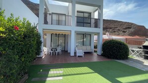 Un edificio a due piani con un balcone, un patio con mobili da esterno e vista su un paesaggio montuoso.