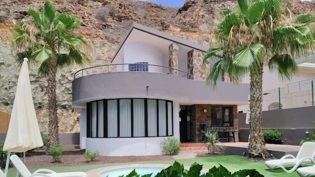 Una villa moderna con piscina, immersa tra palme e un paesaggio roccioso.