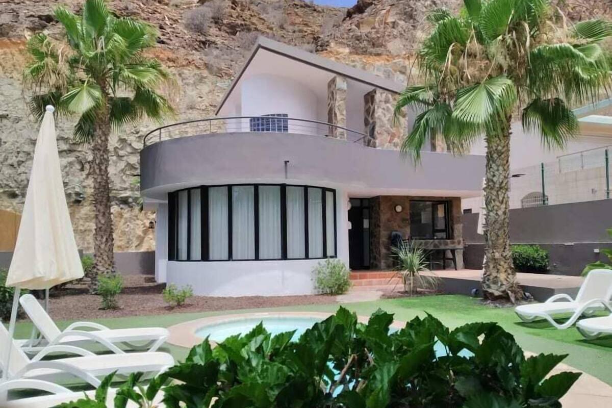 Une villa moderne dotée d’une piscine, entourée de palmiers et d’un paysage rocheux.