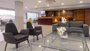 Una hall moderna di un hotel con una reception, un'area relax e vista sulla città.