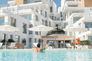 A modern hotel with a swimming pool, sun loungers, and umbrellas.
