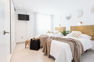 A modern hotel room with two beds, a flat-screen TV, a large window with curtains, and a wall with decorative moon and crescent shapes.