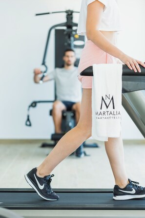 Una persona che cammina su un tapis roulant in palestra, con attrezzature per esercizi sullo sfondo.