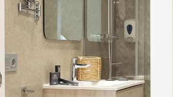 A modern bathroom with a wooden vanity, a glass shower enclosure, a round mirror, and a towel rack.