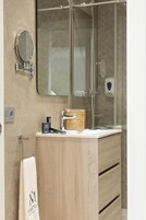 A modern bathroom with a wooden vanity, a glass shower enclosure, a round mirror, and a towel rack.