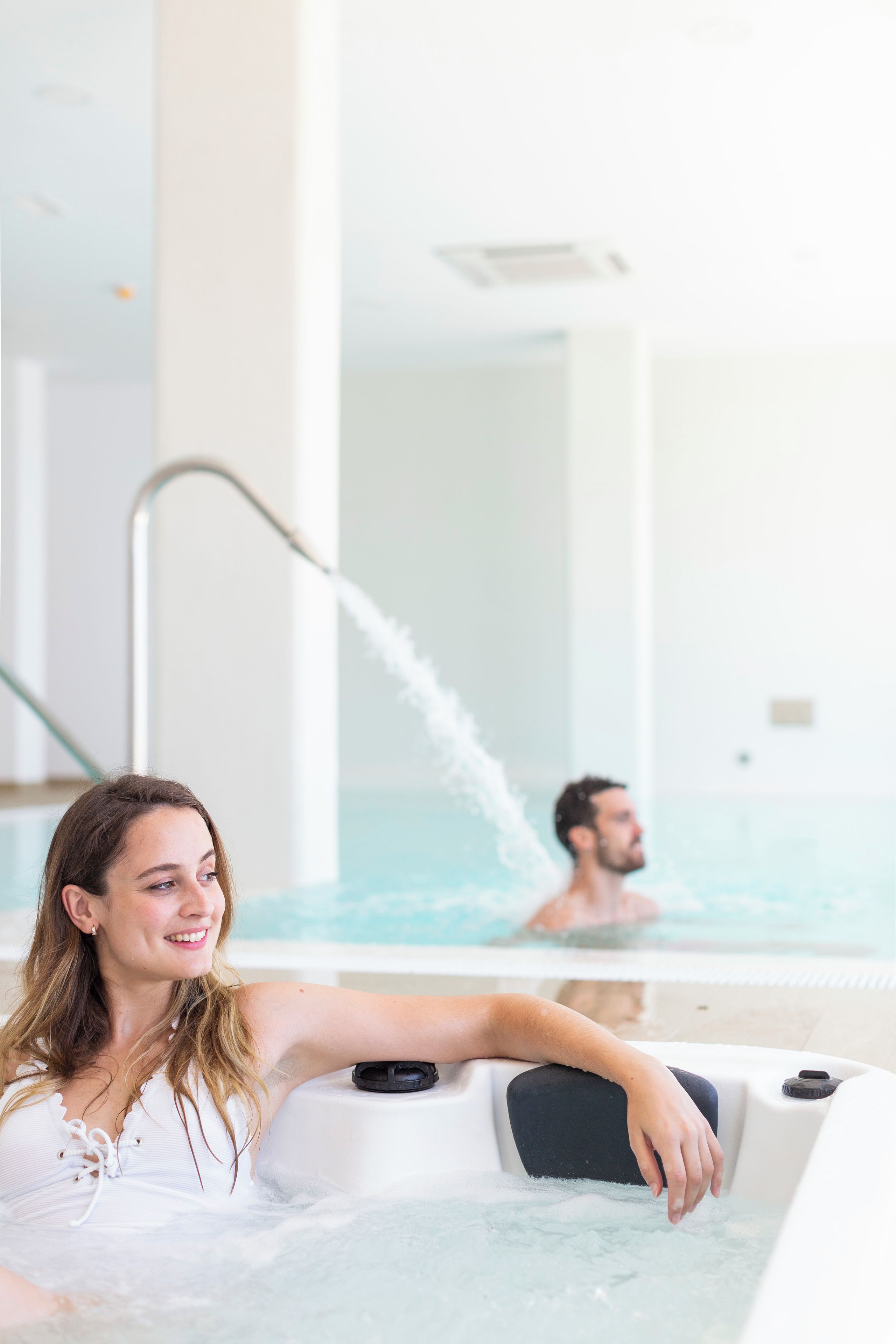 En kvinna som kopplar av i ett bubbelbad, med en man i bakgrunden.