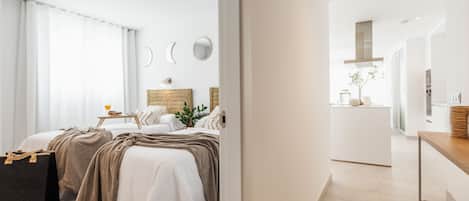 Een moderne hotelkamer met twee bedden, een kleine kitchenette en uitzicht op de stad.