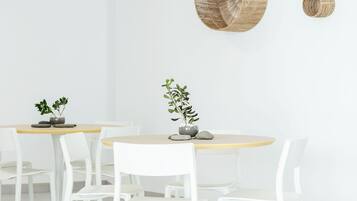 A modern dining area with white chairs and a round table, featuring woven wall art and potted plants.