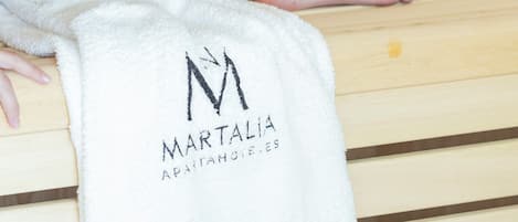 A person sitting on a wooden bench with a towel bearing the 'MARTALIA APARTMENTS' logo.