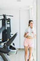Une personne se trouve dans une salle de sport, avec des appareils d’exercice, une fenêtre et un mur blanc.