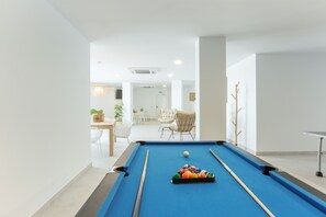 A pool table with balls and cues in a room with a white interior, a dining area, and a chair. - Apartamentos Martalia Nerja (Torrox)