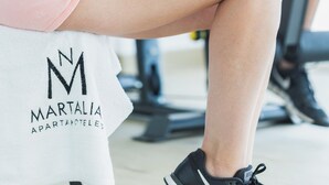 A person exercising with a dumbbell, wearing a white top and pink shorts, with a gym setting in the background. - Apartamentos Martalia Nerja (Torrox)