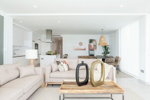 Un salon moderne avec un canapé, une table basse agrémentée d’objets décoratifs et un coin repas avec des chaises en osier.