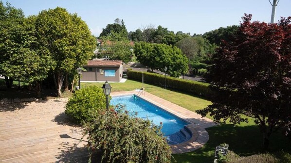 A swimming pool with a wooden deck, surrounded by greenery and a small building. - Snö Pazo de Adran (Teo)