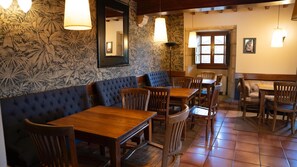 A restaurant interior with wooden tables and chairs, a blue cushioned bench, and floral wallpaper. - Snö Pazo de Adran (Teo)