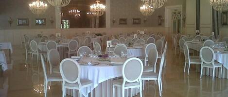 A banquet hall with multiple round tables, white chairs, and chandeliers.