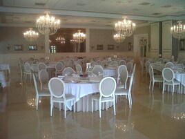 A banquet hall with multiple round tables, white chairs, and chandeliers.