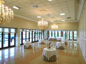 Un vaste hall doté de grandes fenêtres, de lustres et de tables rondes disposées pour les événements.