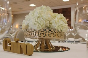 A table setting with a decorative gold and white floral centerpiece, a gold 'CINCO' sign, and wine glasses. - Snö Pazo de Adran (Teo)