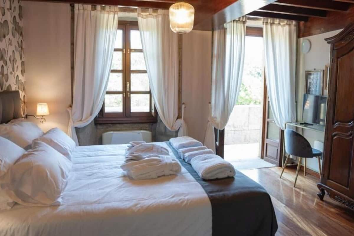A bedroom with a large bed, a wooden wardrobe, and a desk with a chair.
