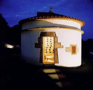 A round building with a white exterior and a red-tiled roof. It features a central door with a cross-shaped window and a small window on the side. - Snö Pazo de Adran (Teo)