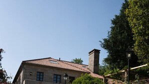 A swimming pool with clear blue water, a stone wall with a lifebuoy, and a building with a tiled roof in the background. - Snö Pazo de Adran (Teo)