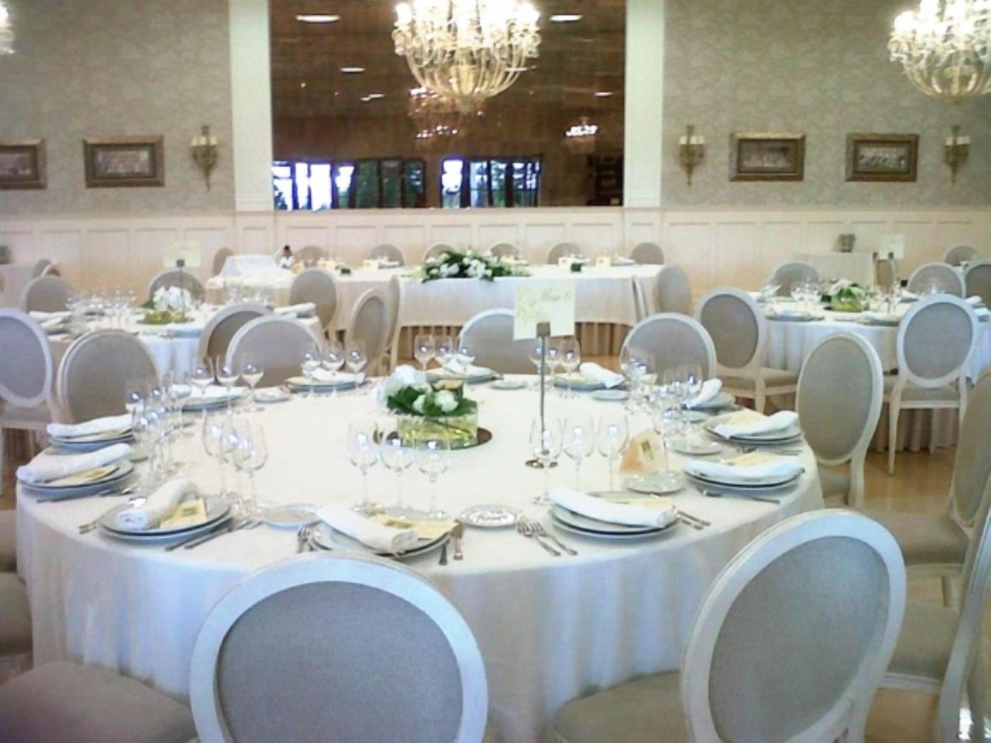Un salón de banquetes con mesas redondas dispuestas para comer, cada una con manteles blancos, sillas y centros de mesa.