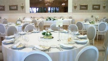 A banquet hall with round tables set for dining, each with white tablecloths, chairs, and centerpieces.