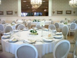 Un salón de banquetes con mesas redondas dispuestas para comer, cada una con manteles blancos, sillas y centros de mesa.