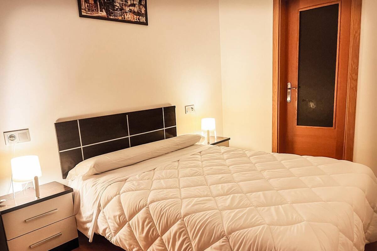 Un lit bien fait, avec une couette blanche matelassée, une tête de lit noire, des tables de chevet avec des lampes et une porte en bois.