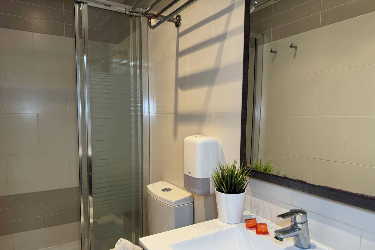 Une salle de bain moderne avec une douche à parois de verre, un lavabo blanc avec un miroir et un distributeur de savon liquide.