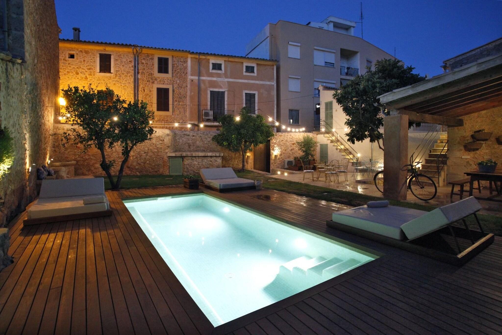 A swimming pool with lounge chairs, a wooden deck, and a stone building in the background.