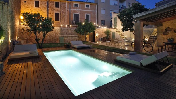 Une piscine avec des chaises longues, une terrasse en bois et un bâtiment en pierre en arrière-plan.
