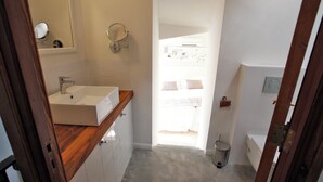 Une salle de bain avec un meuble-lavabo en bois, un miroir rond, un petit lavabo et des toilettes.